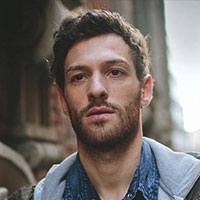 A bearded man in a jacket standing in front of a building.