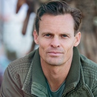Man in green jacket sitting on bench in park.